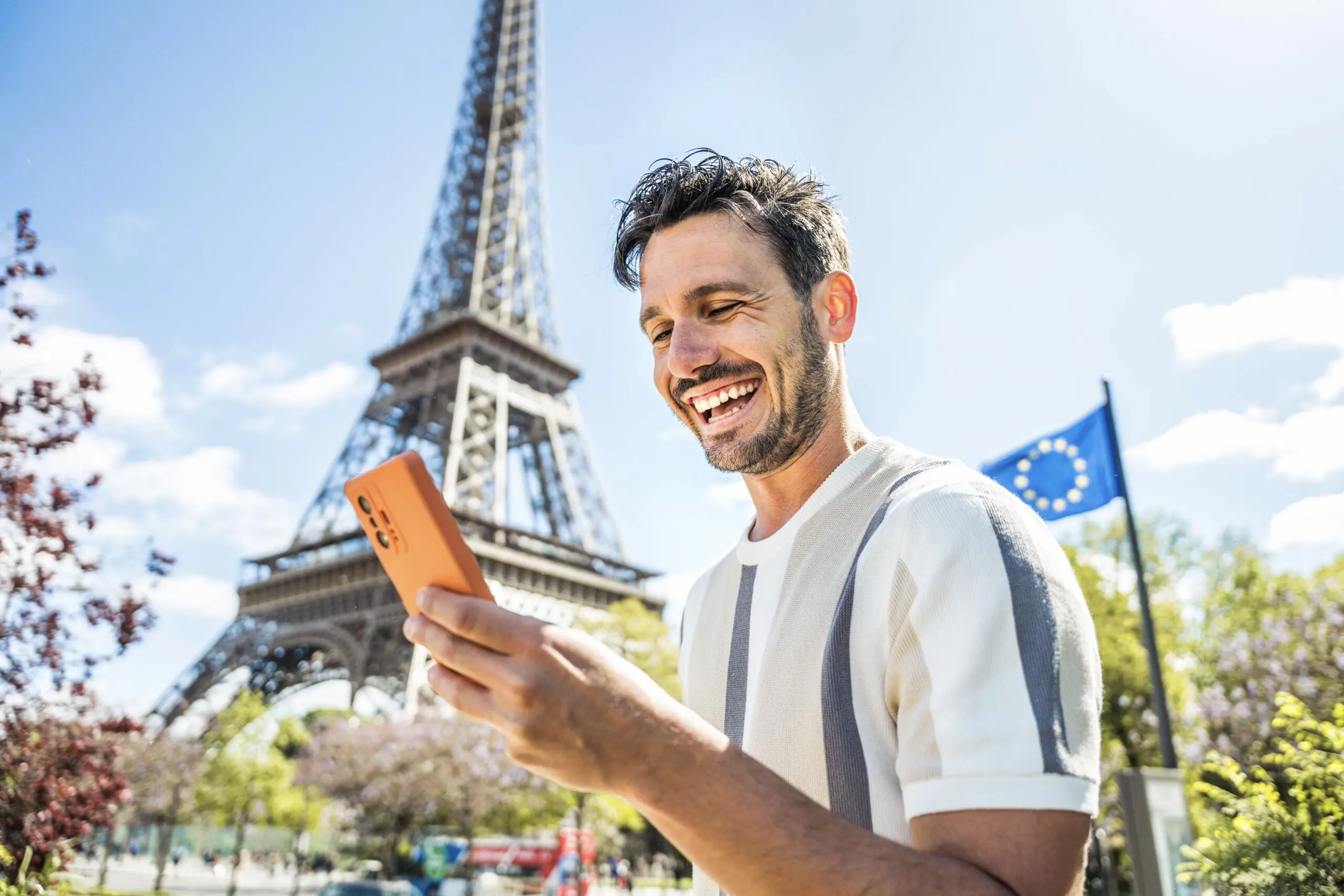 Young entrepreneur holding smartphone in front of Eiffel Tower, France Talent Passport visa