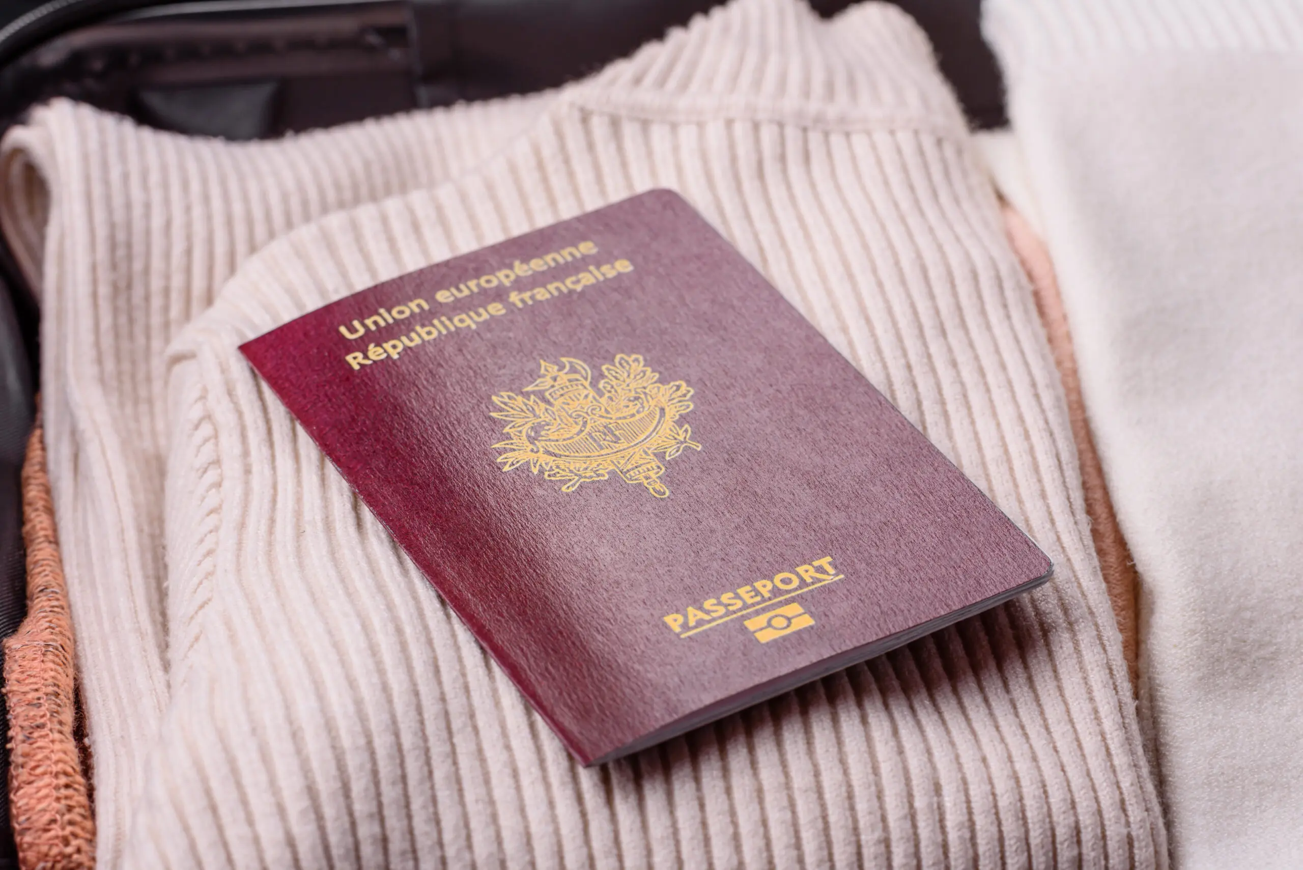 French passport resting on knitted sweaters in a suitcase, illustrating France naturalization