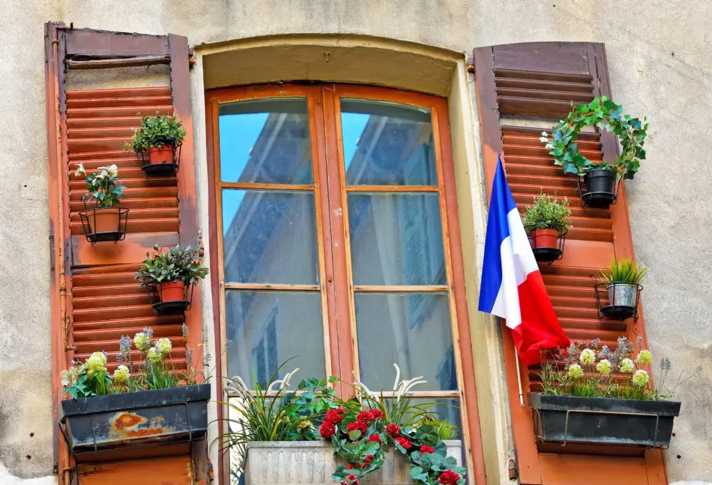 Traditional Provençal window with shutters, potted flowers and a French flag, illustrating living in France