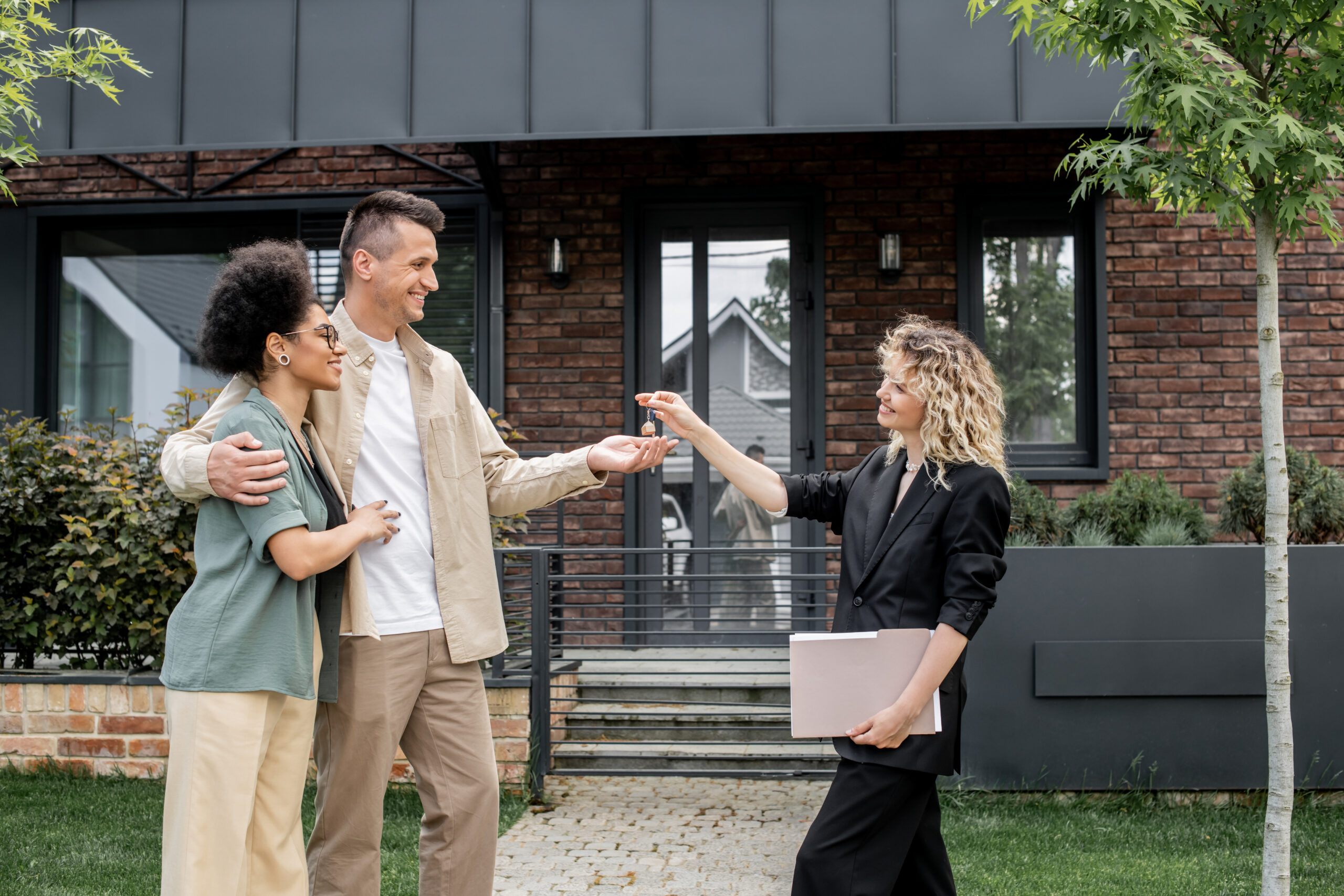 An estate agent handing house keys to a smiling couple outside a home, representing buying property in France as a foreigner